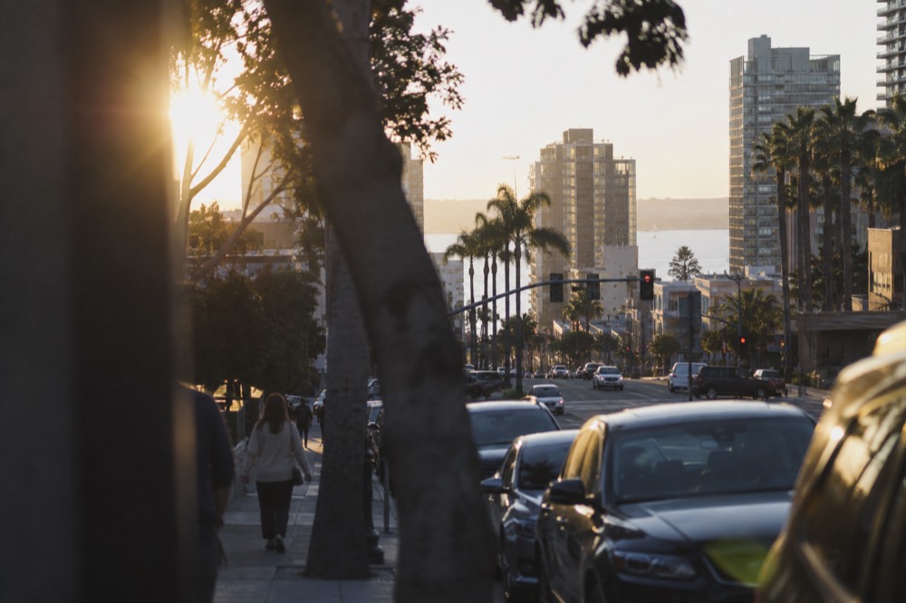 A San Diego city street with traffic signals and parked cars along the curb
