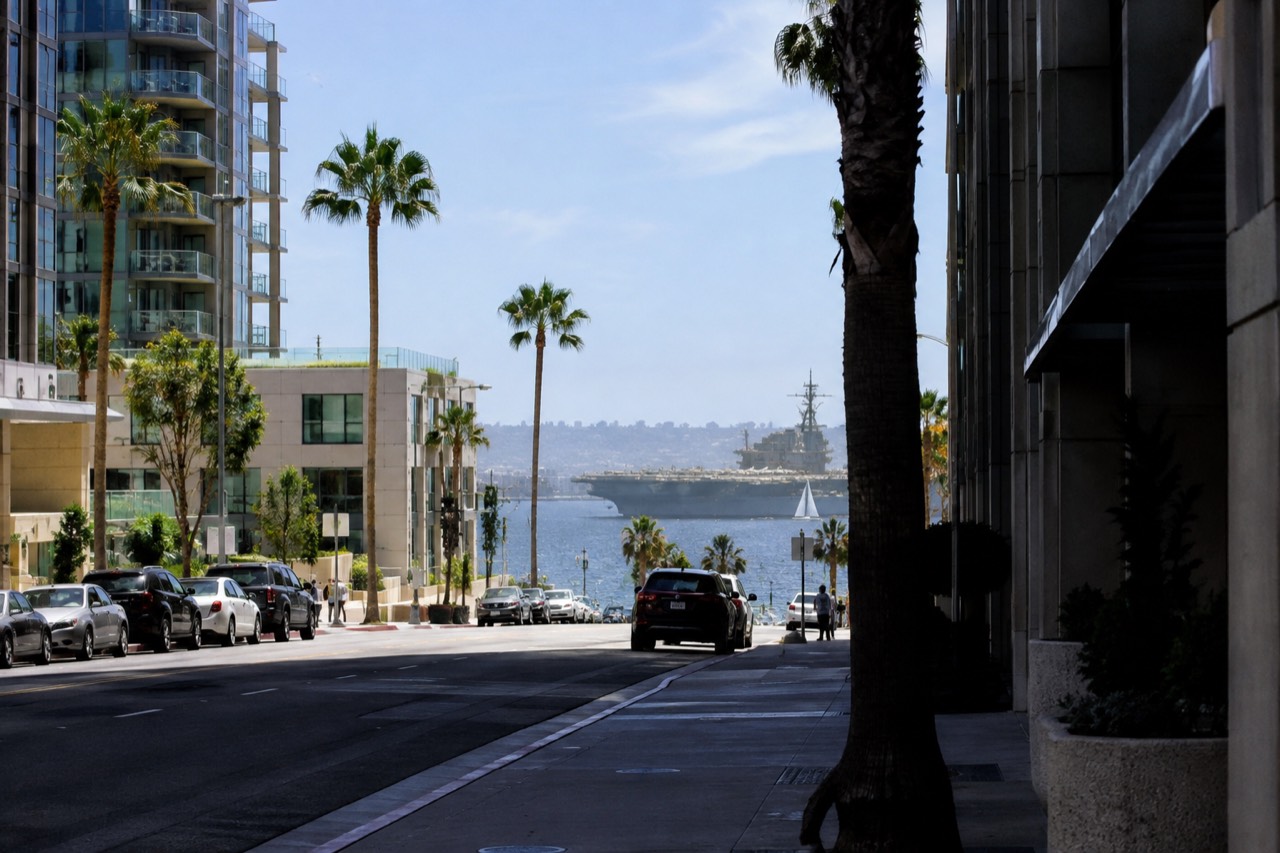 A quiet downtown San Diego street with the USS Midway visible across the bay in the distance