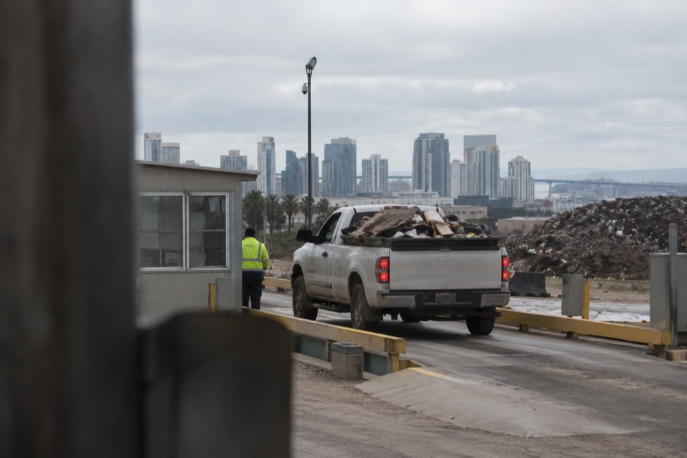A pickup truck crossing a landfill scale while an attendant checks the load