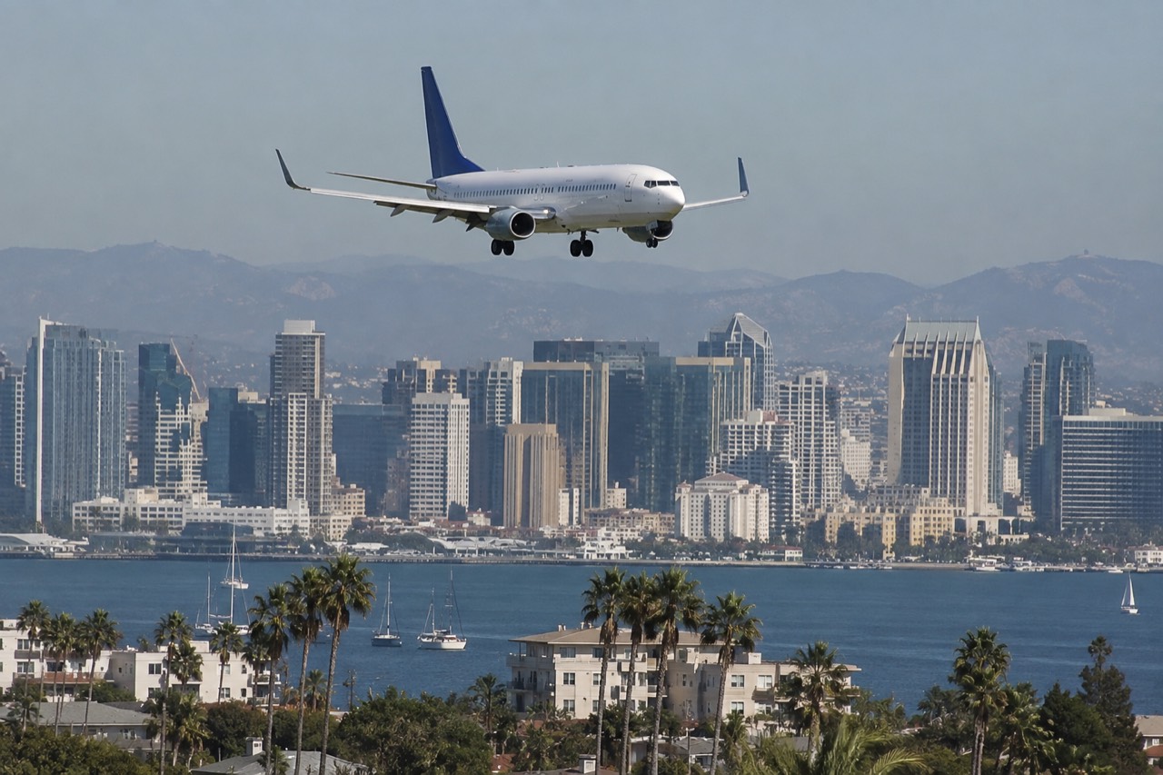 A plane descending over San Diego with the downtown skyline and bay in the background