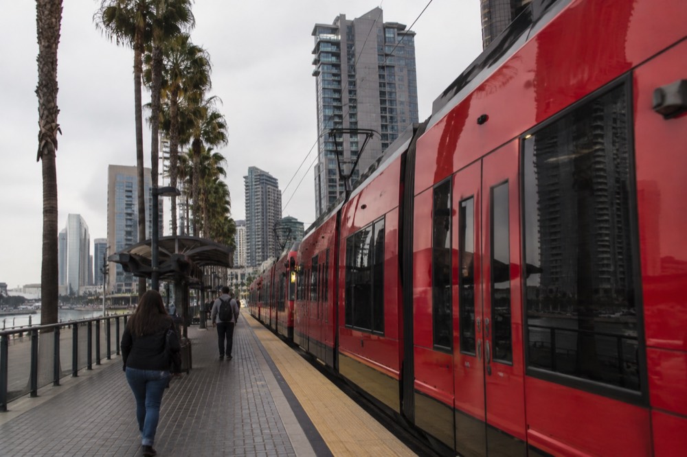 A red San Diego trolley car at a downtown station near the waterfront