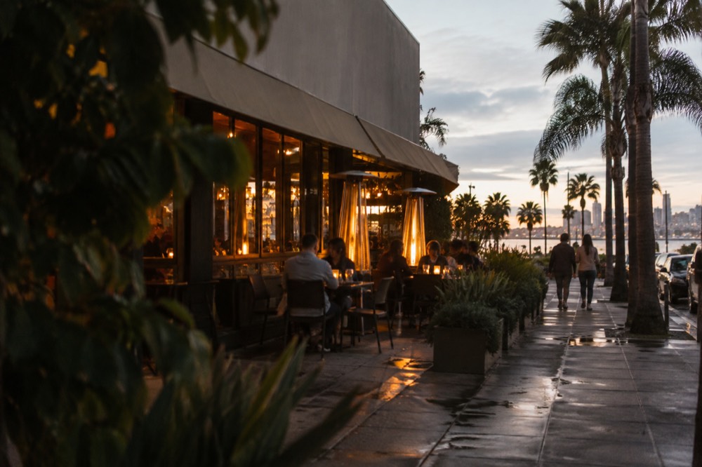 Evening view of a tavern exterior with warm light spilling onto a sidewalk in Coronado