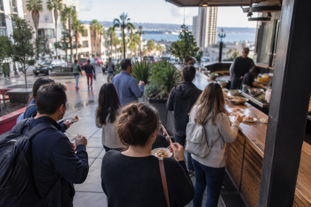 A walking food tour group sampling dishes at an outdoor restaurant counter