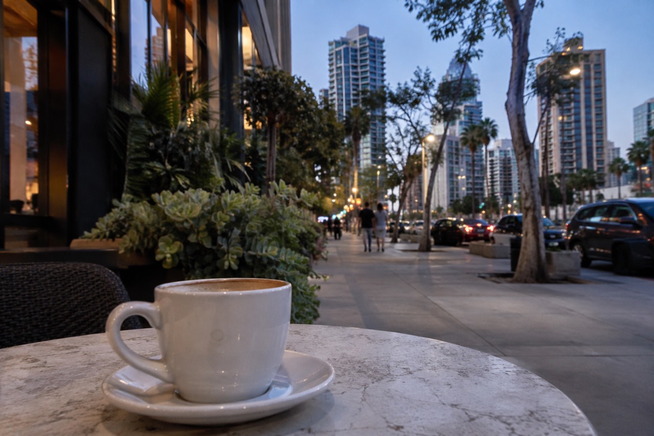 A coffee cup on a sunny sidewalk table beside a leafy San Diego street