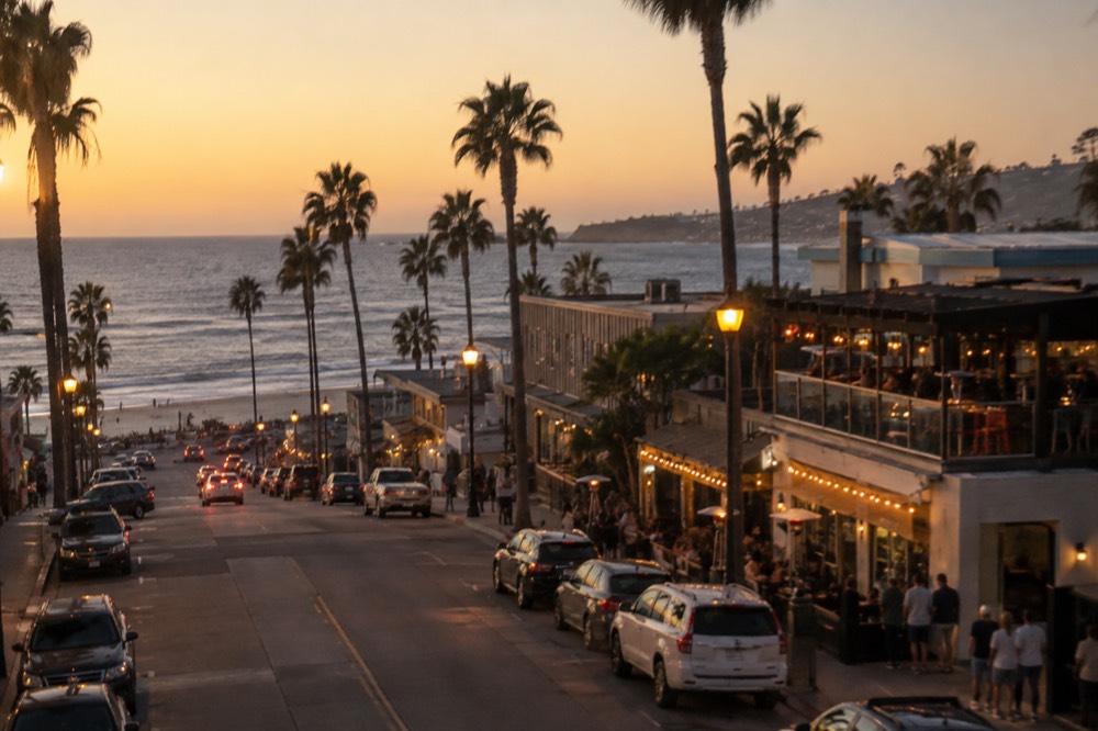 Lit storefronts and palm trees along a Pacific Beach bar street in the evening