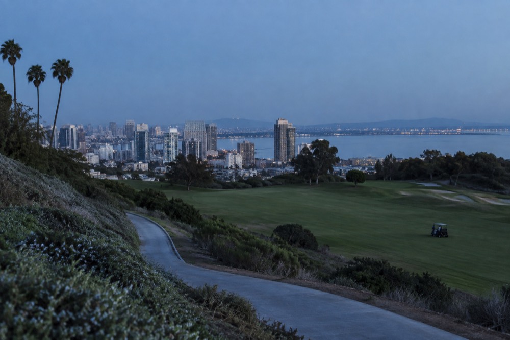 A golf fairway with green hills and coastal shrub under a clear sky