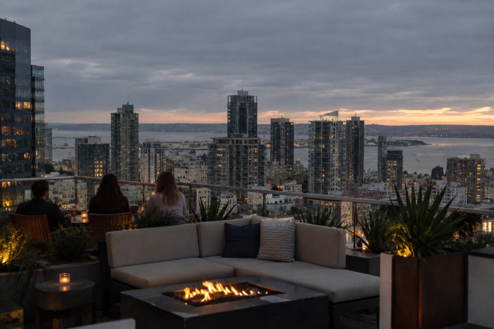 A rooftop patio at dusk overlooking city buildings and a distant bay