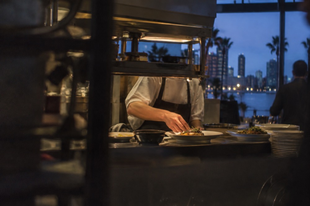 Chef plating a dish at a kitchen pass inside a busy restaurant