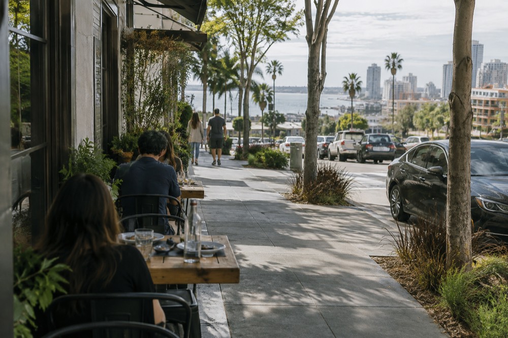 A sidewalk table outside a small restaurant on a tree-lined San Diego street