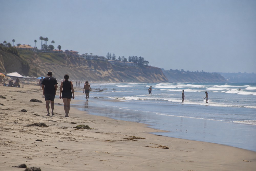 Wide sandy beach in Carlsbad with gentle surf and bluffs in the distance