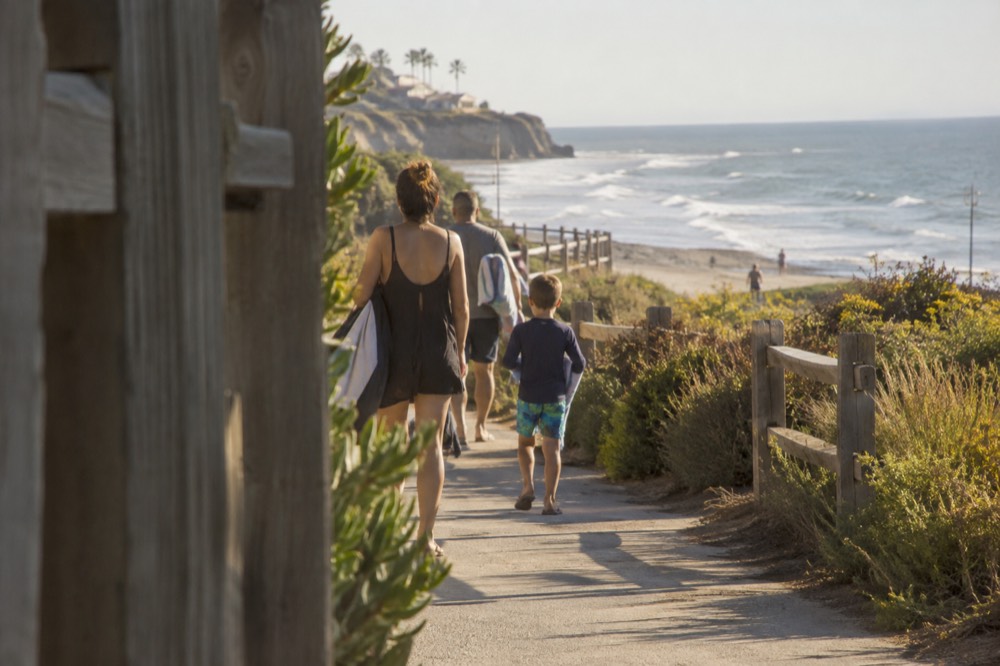 Family walking on a beach boardwalk path in warm evening light