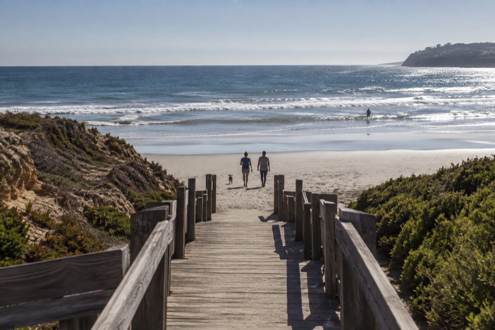 Wooden beachfront walkway leading toward sand and gentle surf in Del Mar