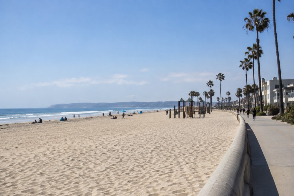 Wide sandy beach with a playground and palm trees near the boardwalk