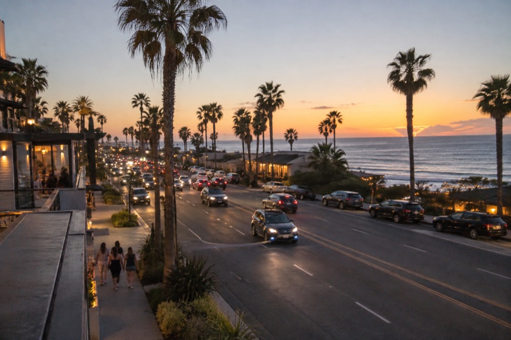 Coastal highway town strip at dusk with storefront lights and palm trees