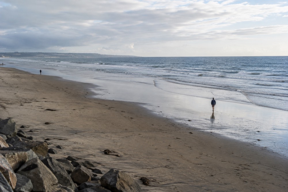 A wide empty beach at low tide with gentle waves and a pale sky