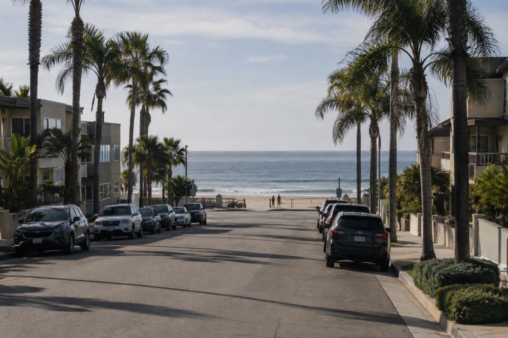 A quiet beachside street with parked cars and palm trees in morning light
