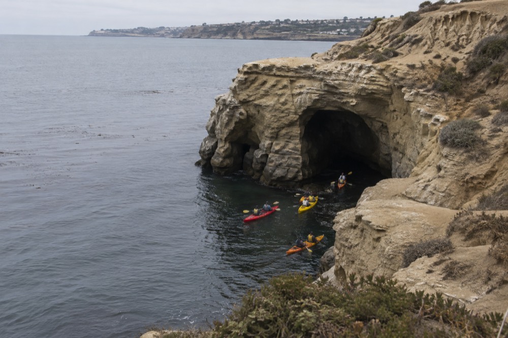 Kayaks paddling along the sandstone cliffs toward a sea cave opening on calm water