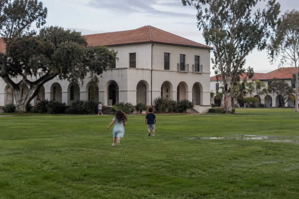 Children playing on a wide green lawn near historic buildings