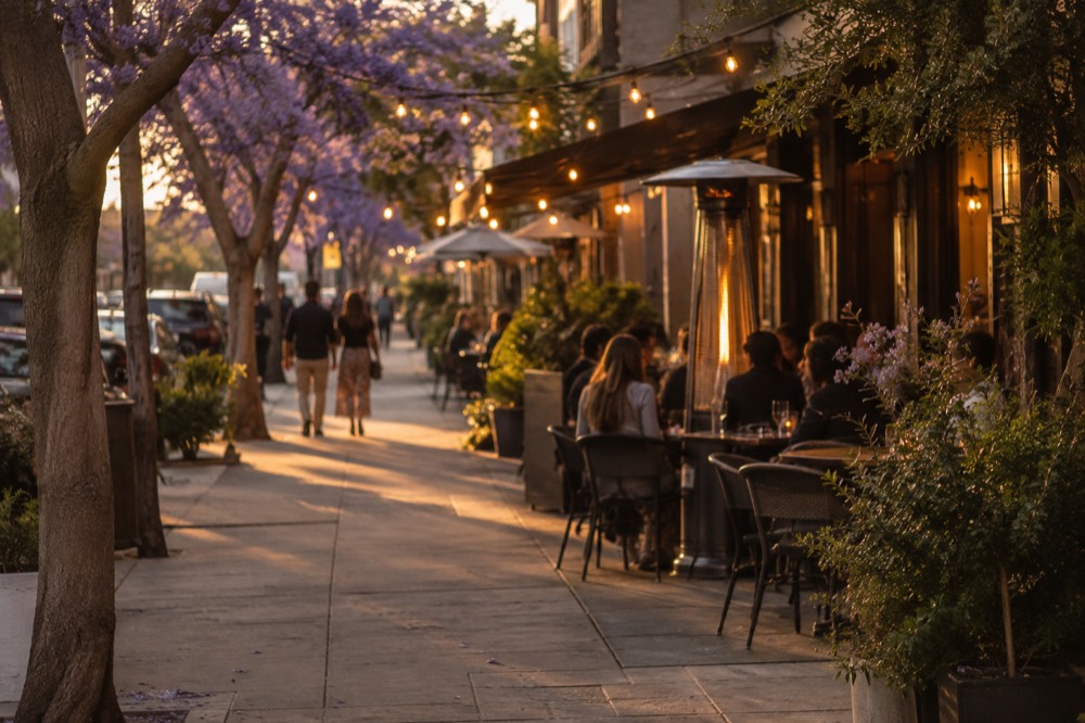 Evening street with string lights above sidewalk tables outside restaurants