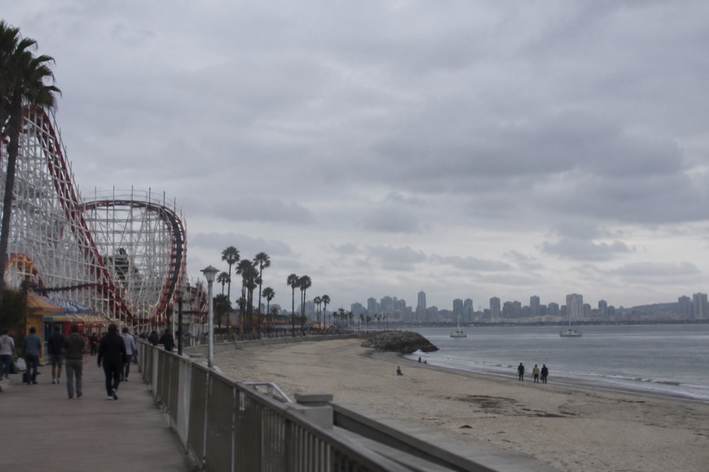 A large theme park beside bay water with roller coaster tracks and a skyline in the distance