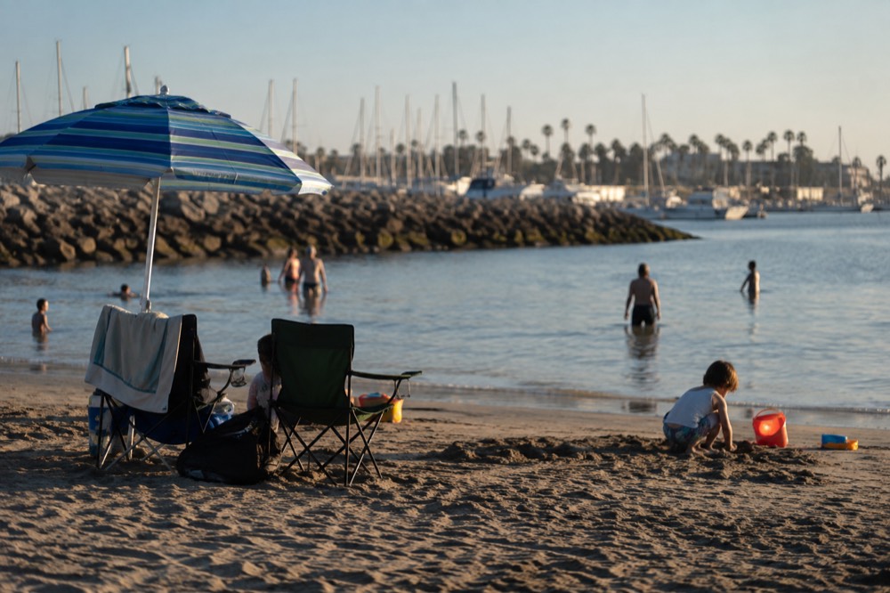 A calm protected harbor beach with gentle shallow water and families set up on the sand