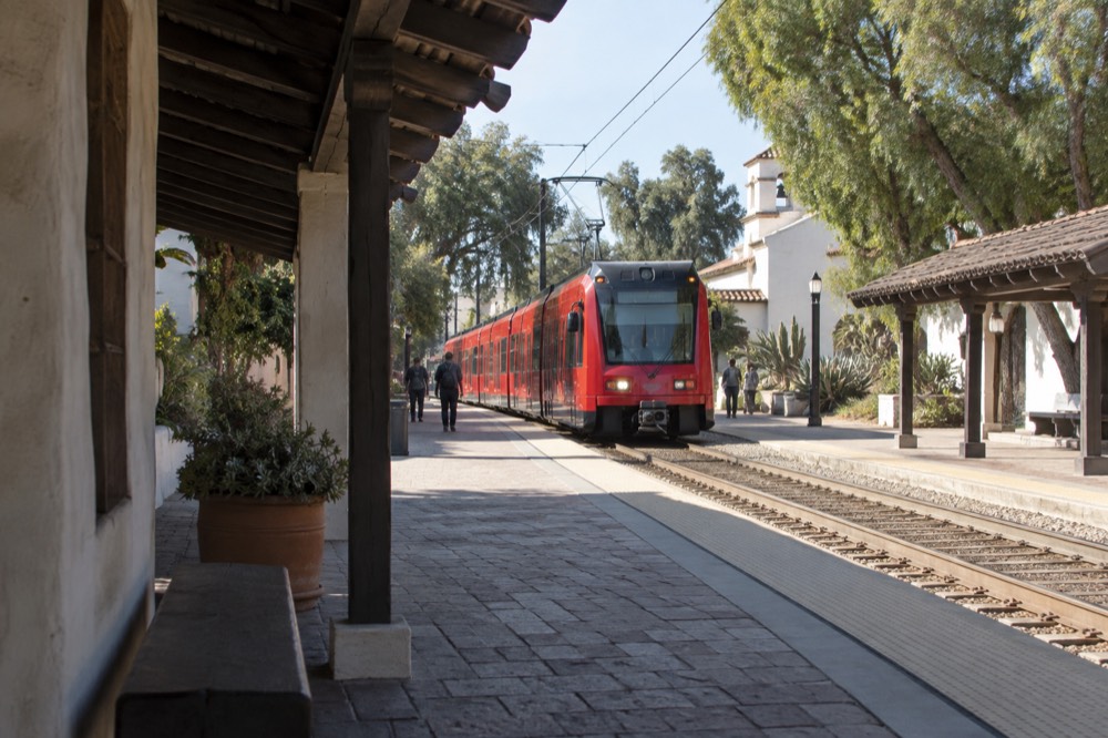 A red San Diego trolley arriving at an open-air transit station