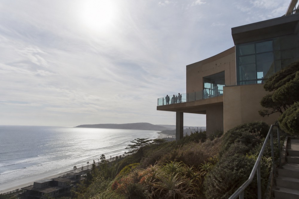 A hilltop aquarium building with an ocean overlook terrace above a curving coastline