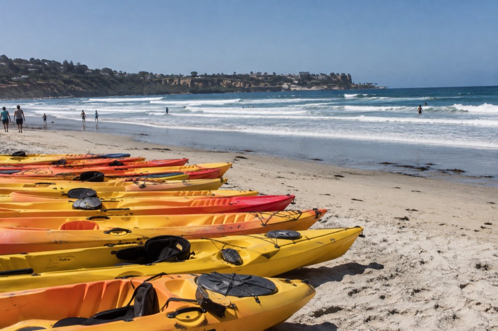Kayaks lined up on a sandy beach at La Jolla Shores with ocean and cliffs in the distance