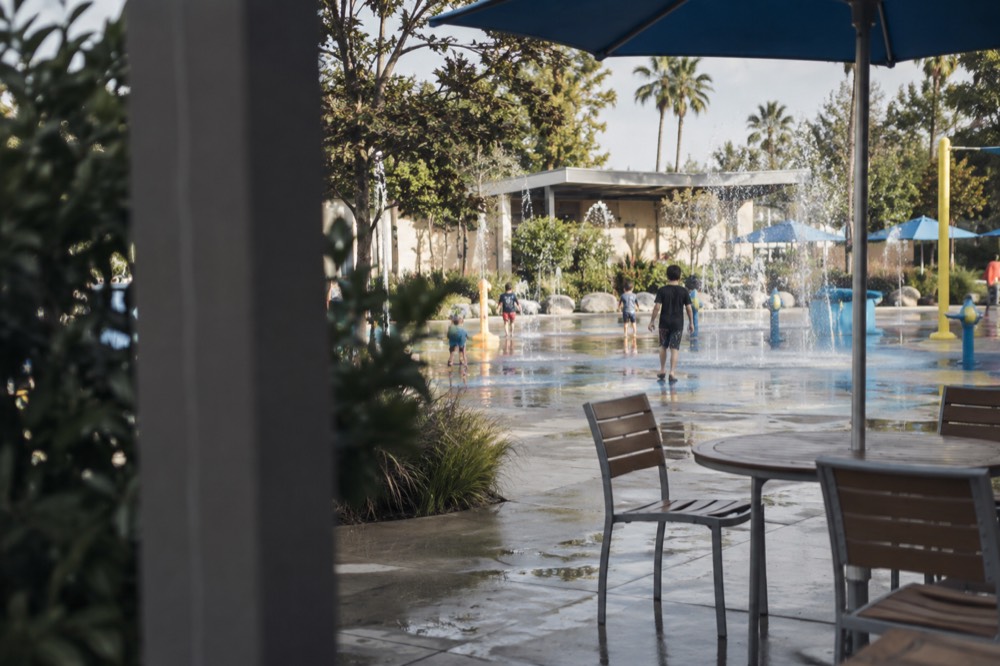 Water play area with fountains and shallow splash pools beside a shaded seating area