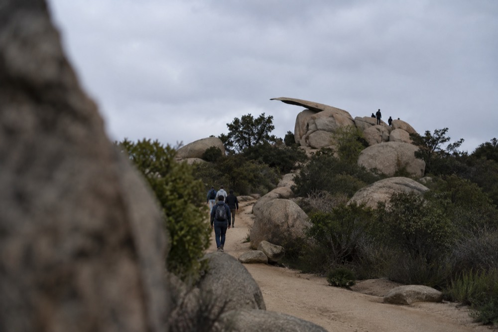 A wide dirt trail climbing through low chaparral toward a rocky ridgeline