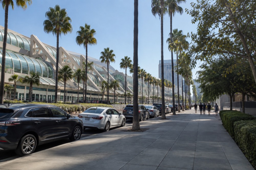 Palm-lined downtown street with parked cars and a large events hall in the distance