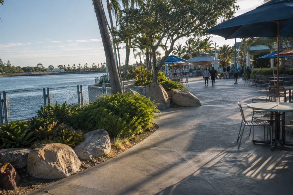 An outdoor eating area with shaded tables and food stands near a park plaza