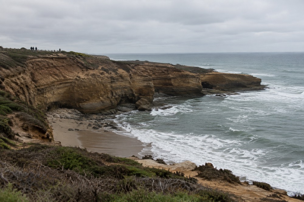 Small cove beach at the base of coastal bluffs with waves rolling in