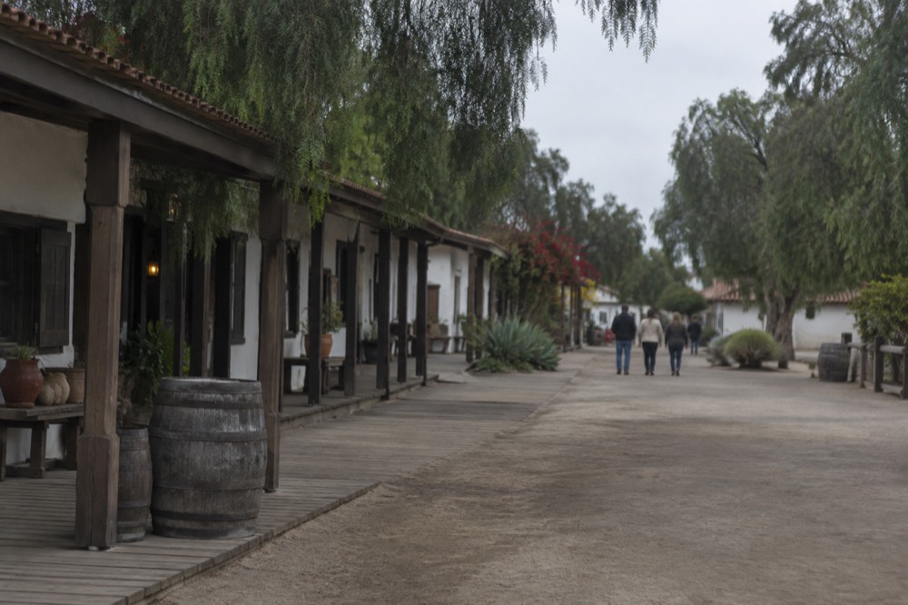 Wooden boardwalk storefronts along a historic Old Town street lined with trees