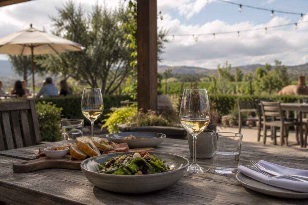 An outdoor patio table set for lunch beneath string lights near a tasting room