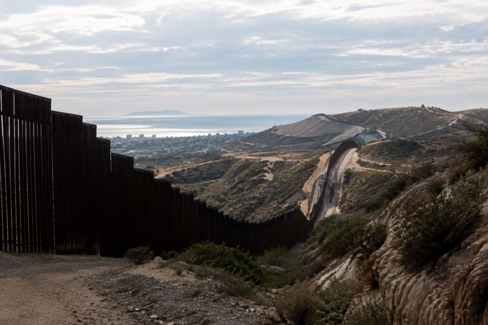 Border fence line rolling over coastal hills under a partly cloudy sky