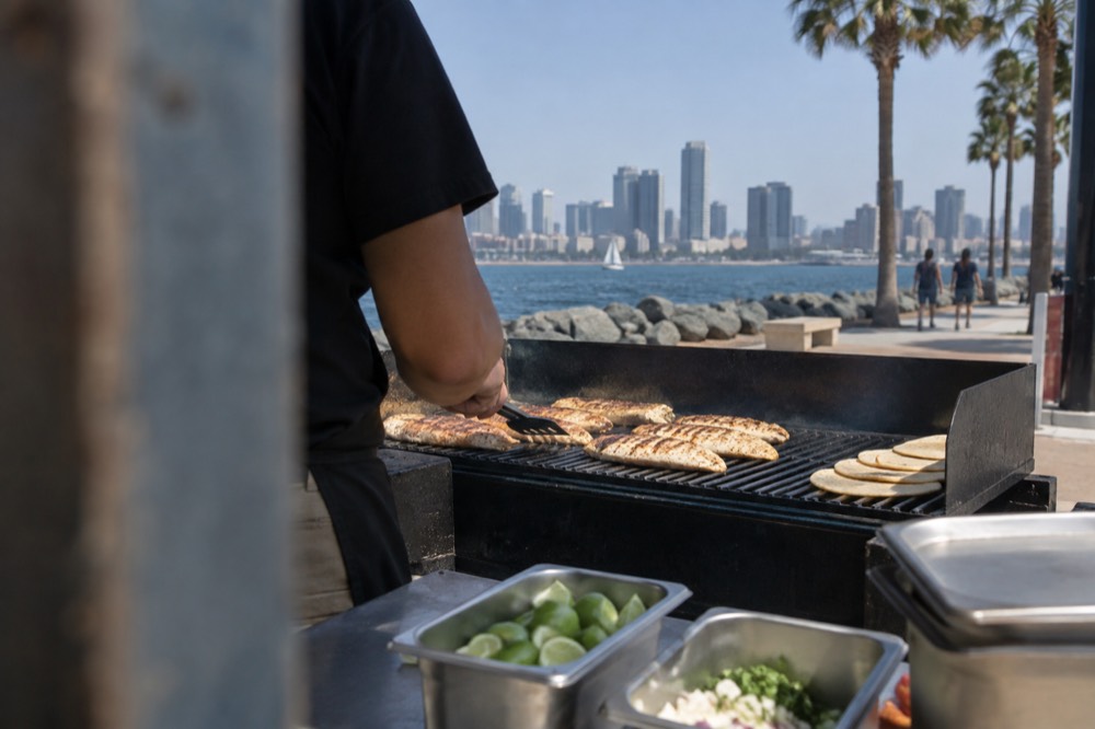 Grilled fish fillets cooking on an outdoor grill beside lime wedges and tortillas