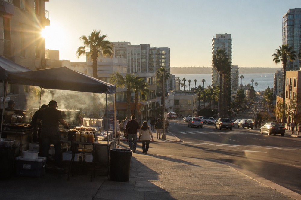 A street corner taco stand with a grill smoking in daylight
