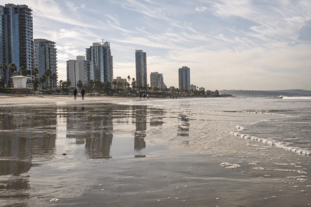 Wide flat beach at low tide with shallow water and distant lifeguard tower