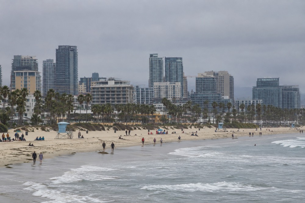 A wide beach with gentle waves and families spread out along the sand near a lifeguard tower