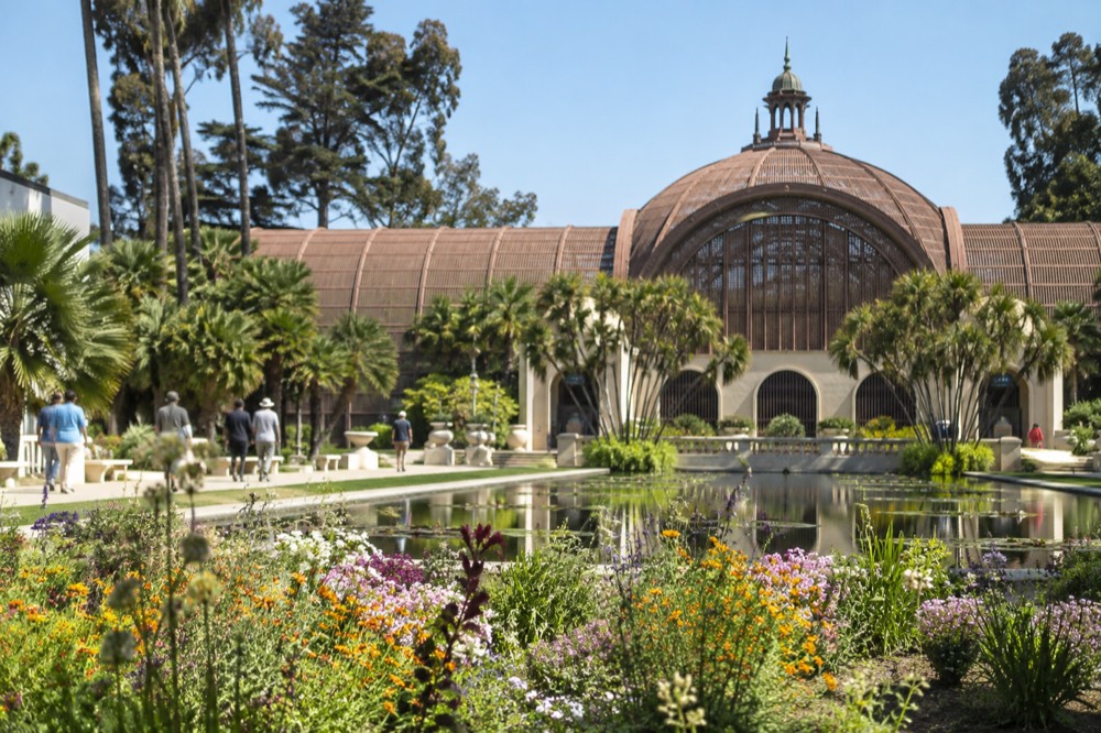 Flower beds and a lily pond in front of a lattice-roofed botanical building in a park