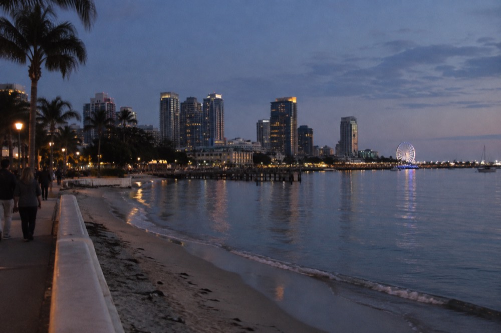 A calm shallow bay with a sandy beach and a distant ferris wheel across the water