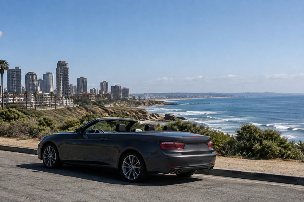 A parked convertible with the roof down on a coastal road overlooking the ocean