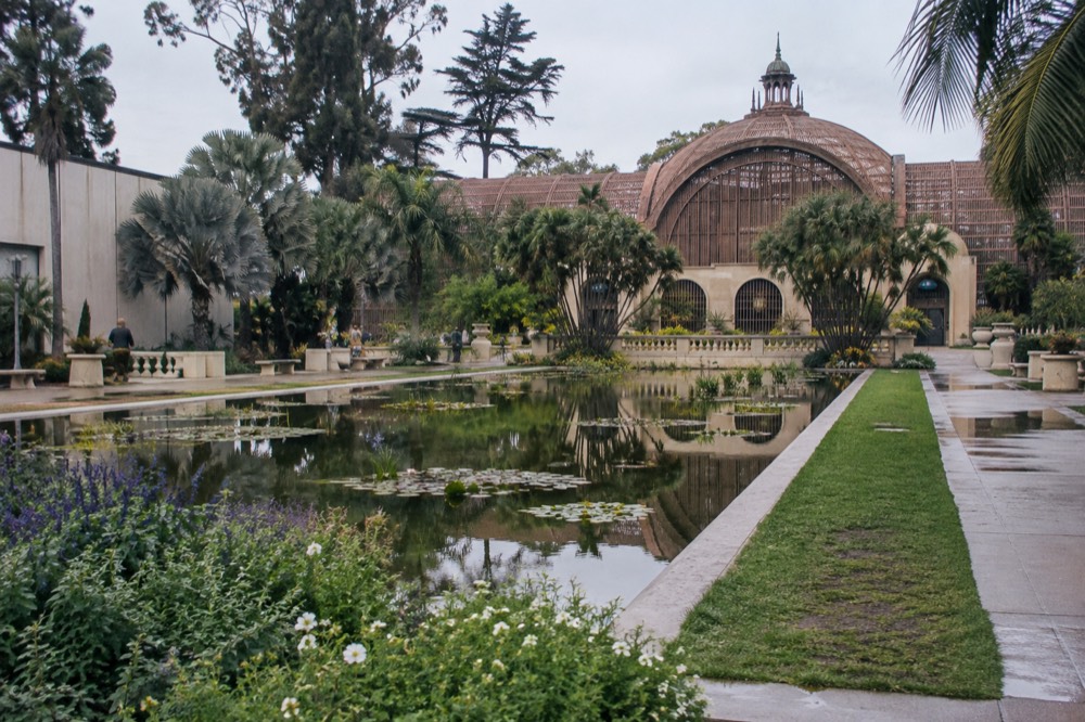 A lily pond in front of a lattice botanical building with reflected greenery
