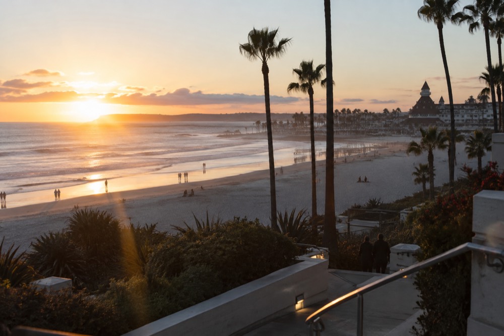 A wide sandy beach at dusk with a historic wooden hotel silhouette in the background