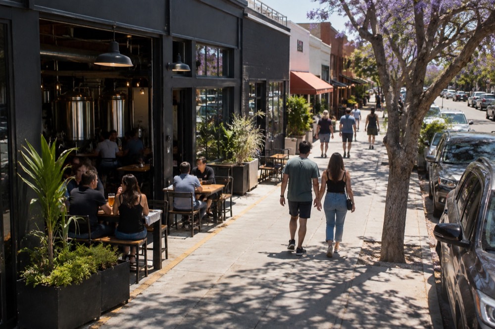 A row of brewery storefronts with patrons walking along a sunny neighborhood street