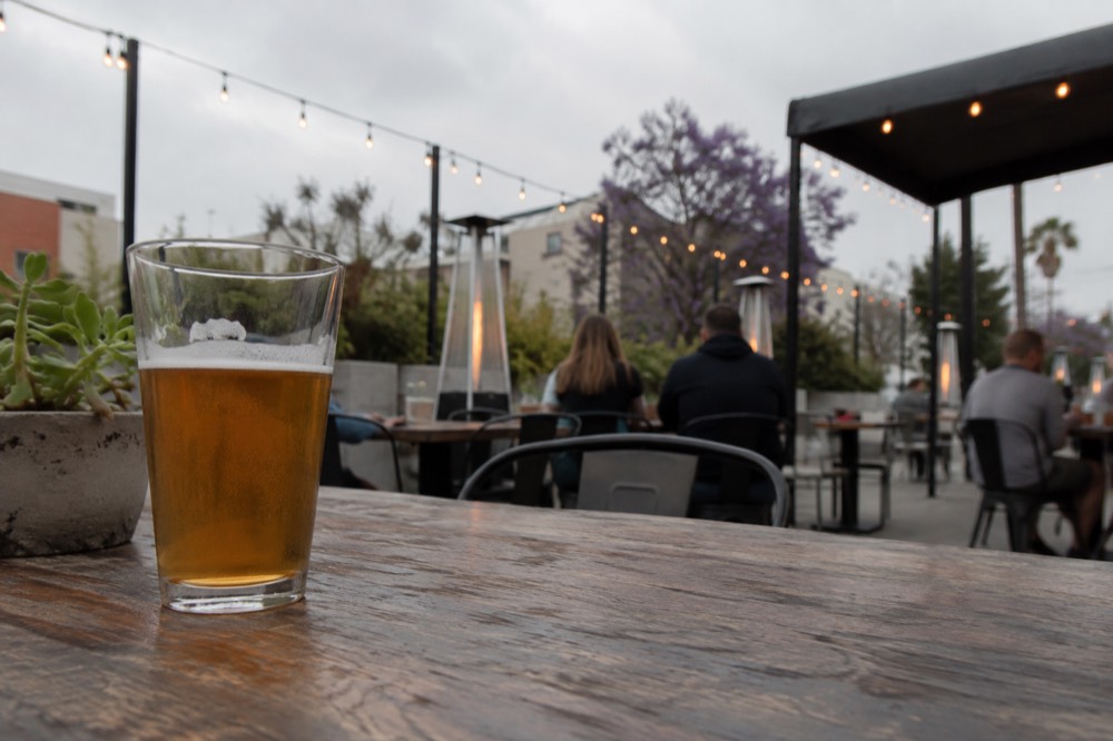 An outdoor brewery patio with string lights and small tables in late afternoon light