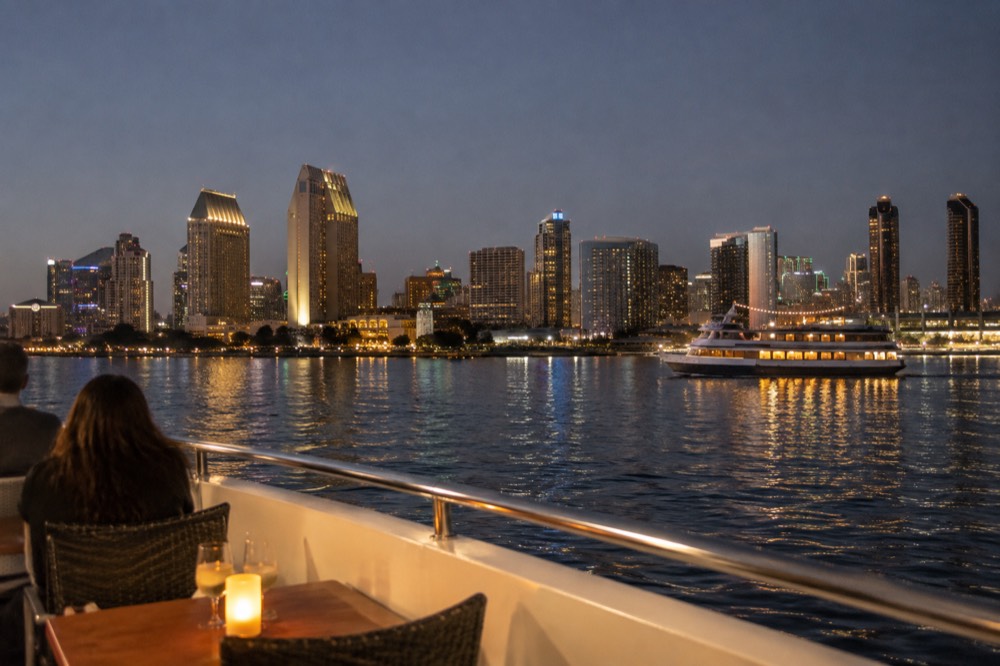 A dinner cruise boat passing city lights across a calm harbor at night