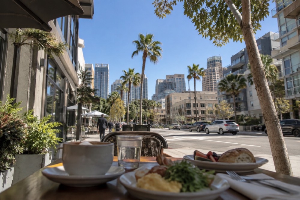 A sidewalk cafe table with coffee and breakfast plates in a sunny San Diego neighborhood