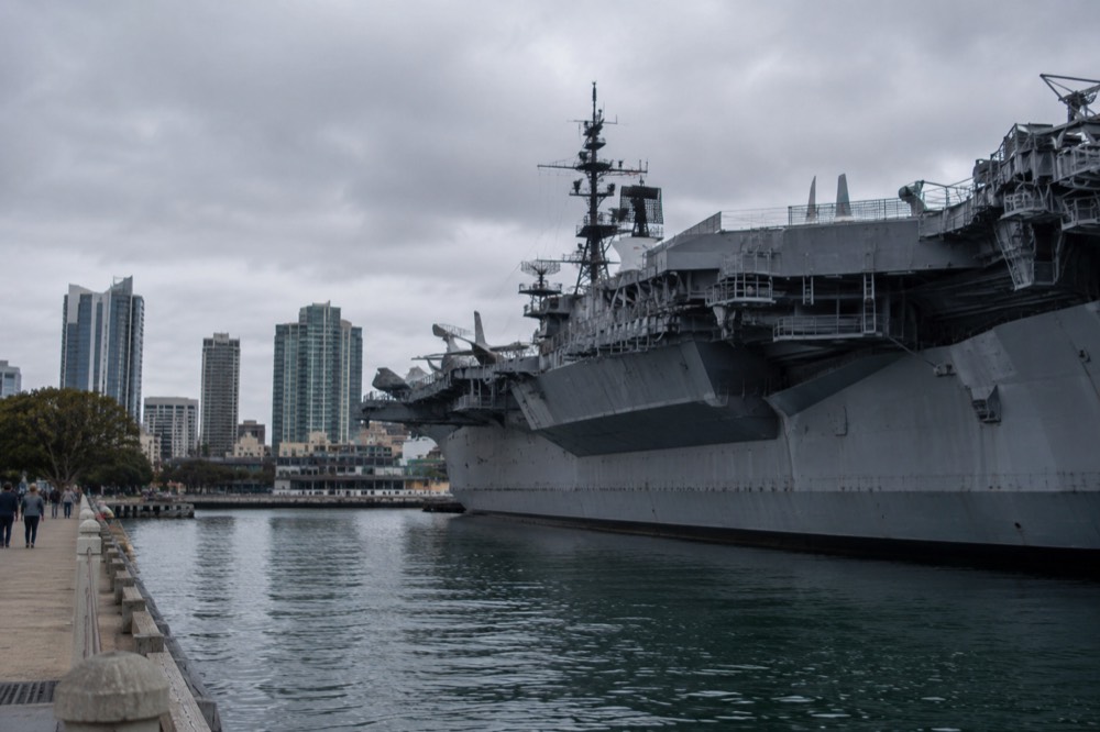Historic aircraft carrier moored at a downtown waterfront with city buildings behind
